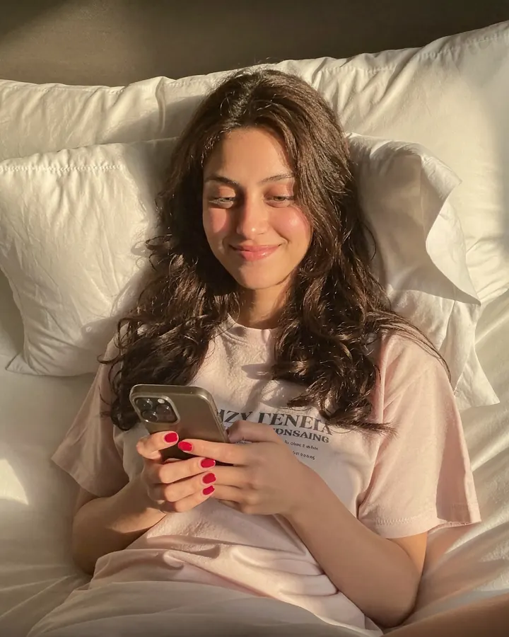 Aisha in bed in the morning light, smiling at her phone as she types