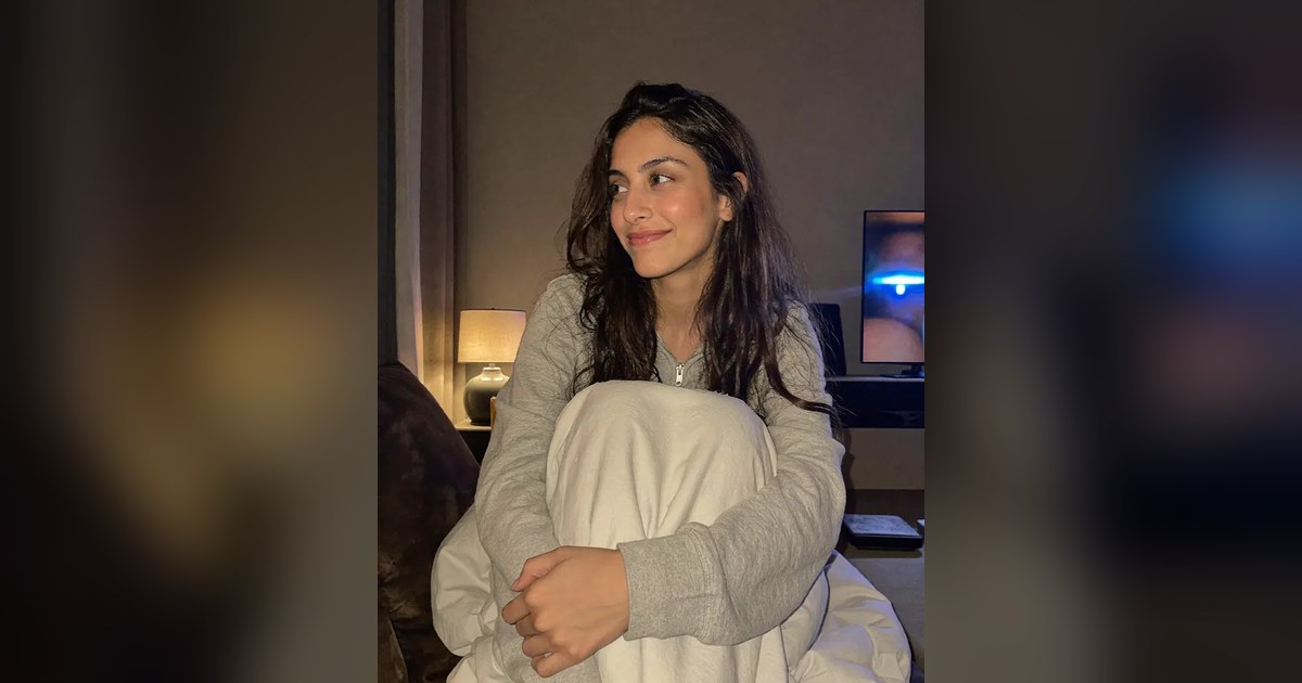 Aisha curled up on a sofa at night, smiling, with a lamp and a TV glowing behind her